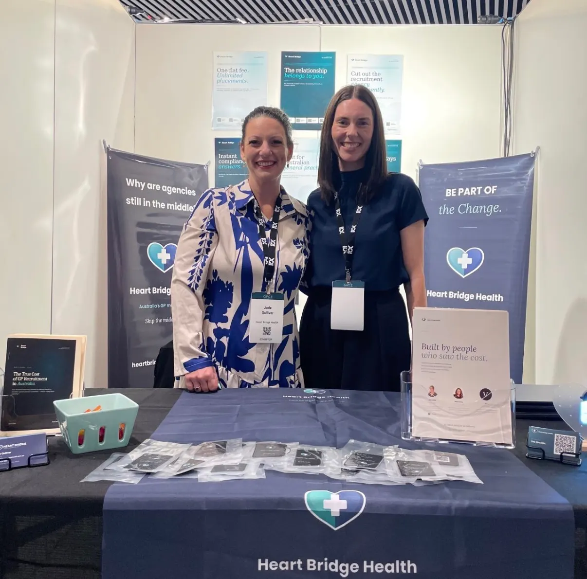 Two members of the Heart Bridge Health team behind their branded stand table
